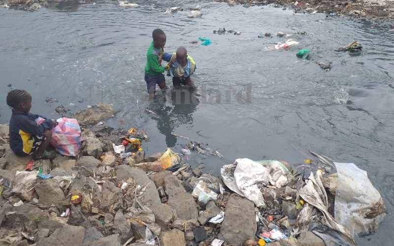 A young boy crosses a 'river of sewer' with his sister on his back
