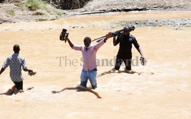 Journalists wade through flooded river Kagir